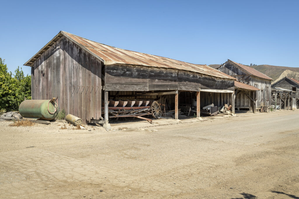 Rustic wooden buildings along a dusty street in a historical town with clear blue sky.