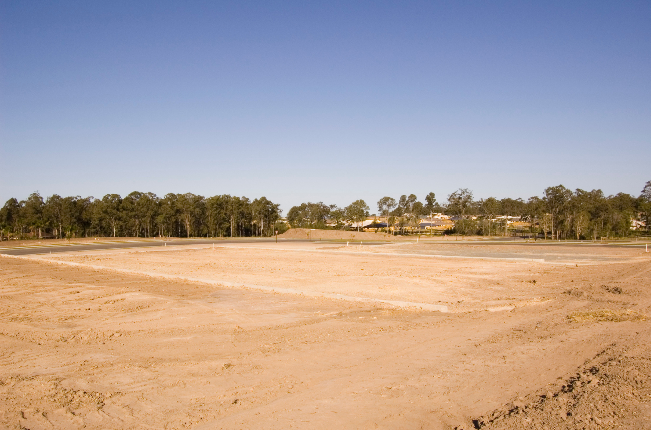 Open field of dirt with a tree line in the background under a clear blue sky.