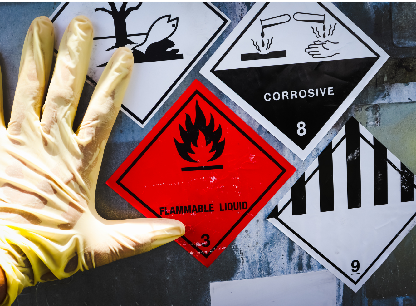 A gloved hand next to various hazard warning signs, including a “Flammable Liquid” label.