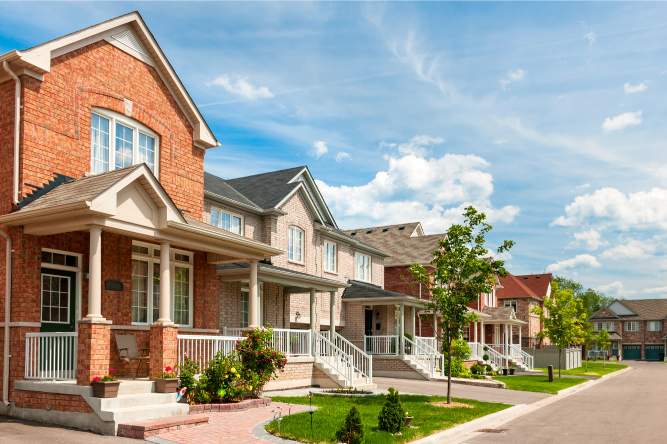 Row of modern suburban houses with front porches, green lawns, and a clear blue sky.