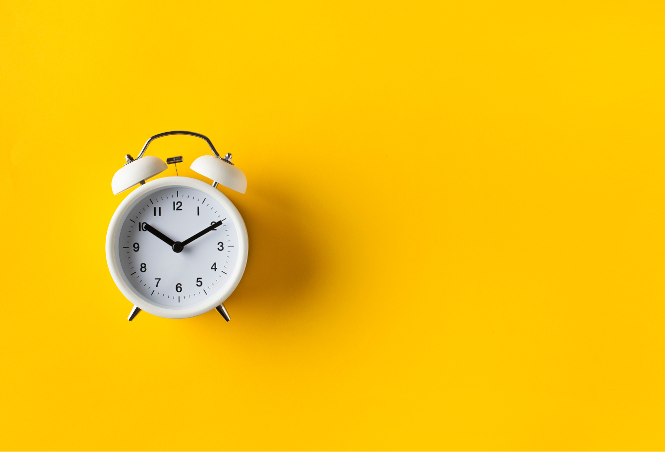 A white clock laying on a yellow background.