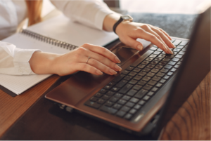 Person typing on a laptop with a notebook beside them.