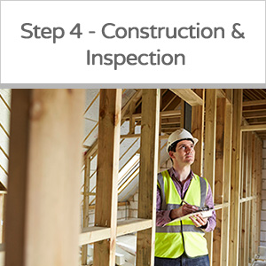 A construction inspector in a safety vest and hard hat inspecting a framed building under construction.