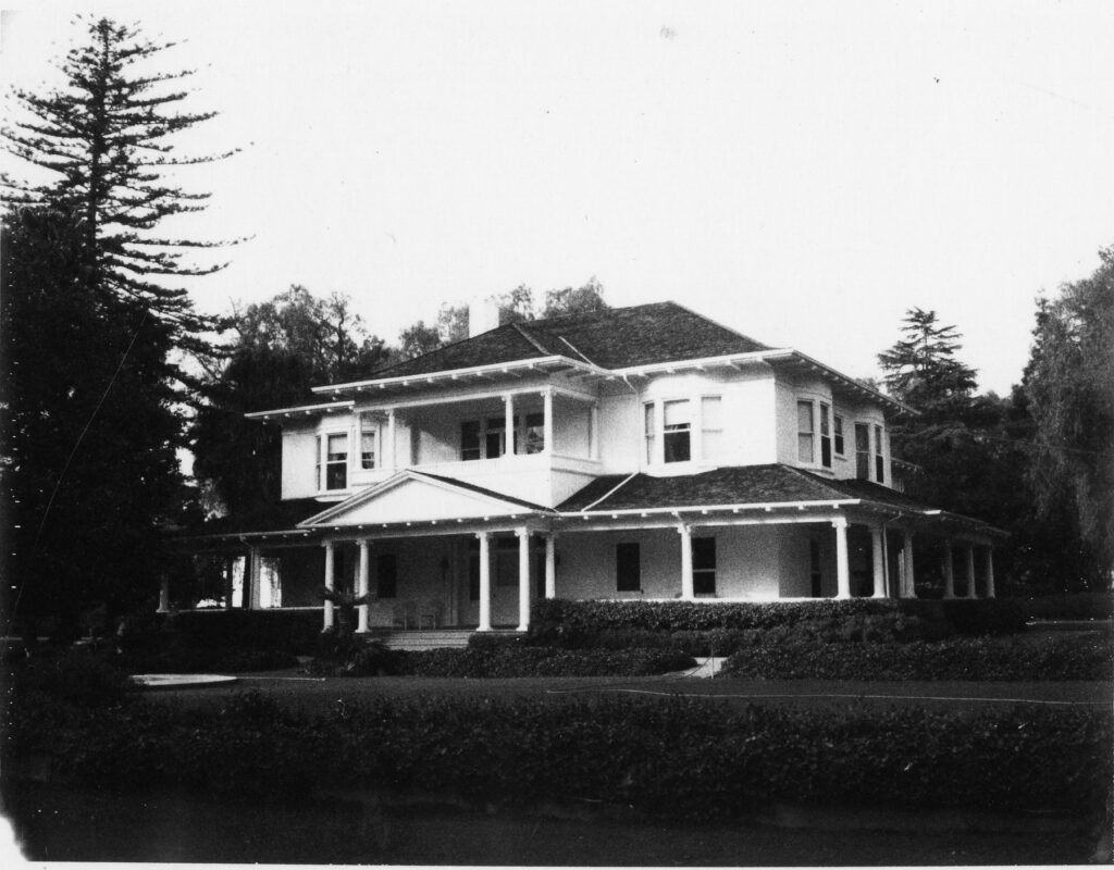 Black and white photo of the two-story Lloyd-Butler House with wraparound porch and surrounding trees.