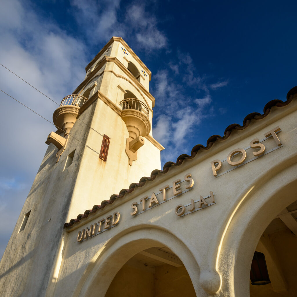 Upward view of the Ojai Post Office Tower and Portico against a blue sky, emphasizing its arches and architectural details.