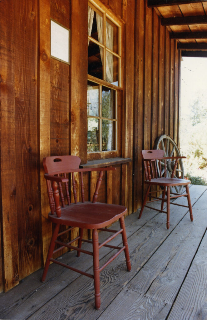 Wooden porch of the Stagecoach Inn with two red chairs and a wagon wheel decoration.