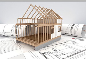 A wooden architectural model of a building under construction on top of rolled architectural blueprints.