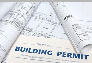 Rolled blueprints and a printed building permit document, symbolizing building permitting and review process.