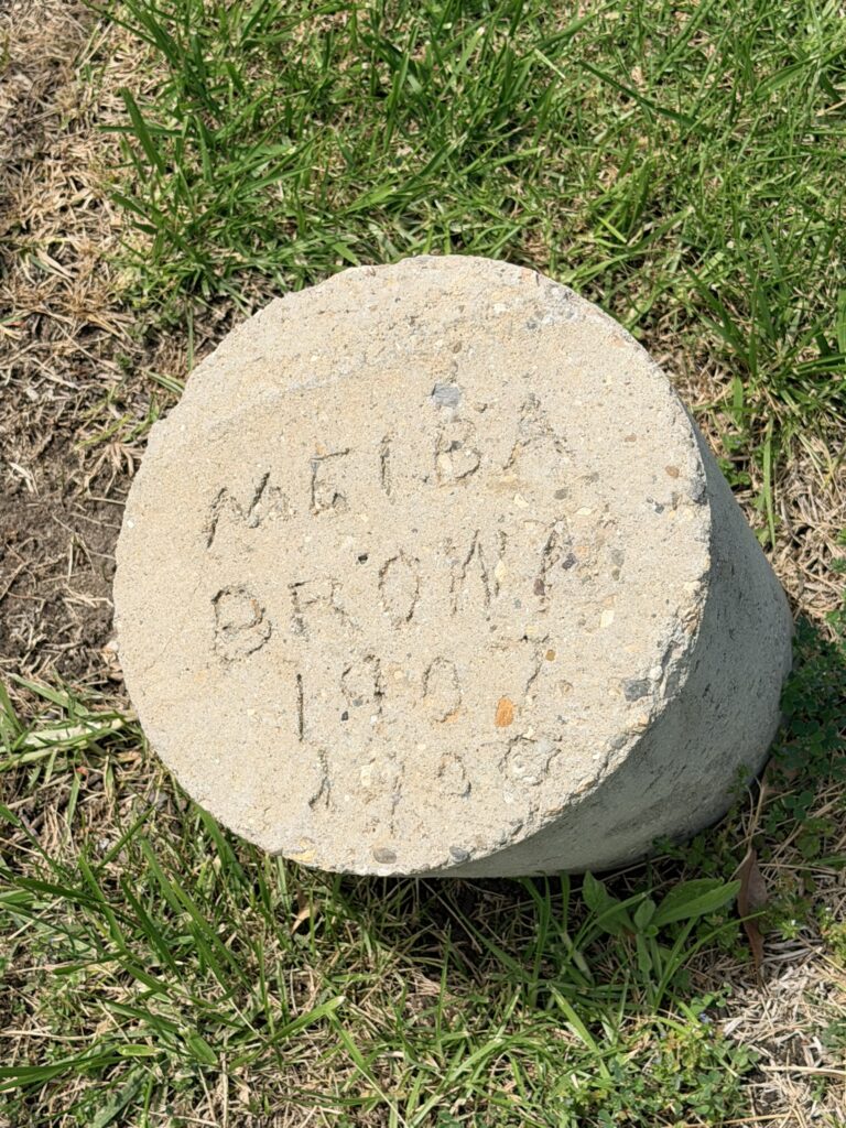 Concrete cylindrical headstone with handwritten text, dated 2026, resting on grass.