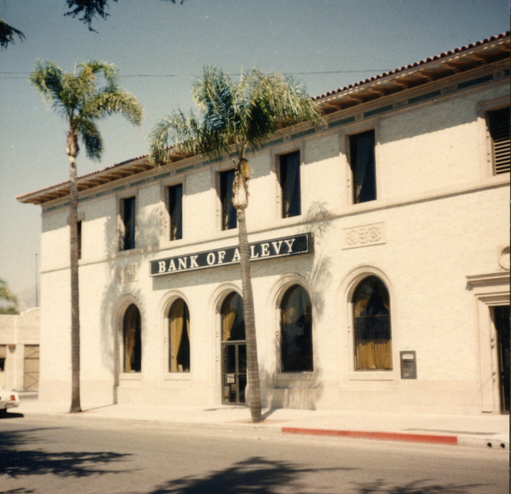 Two-story Fillmore State Bank building from circa 1980s with "BANK OF A LEVY" signage, arched windows, and palm trees in front.