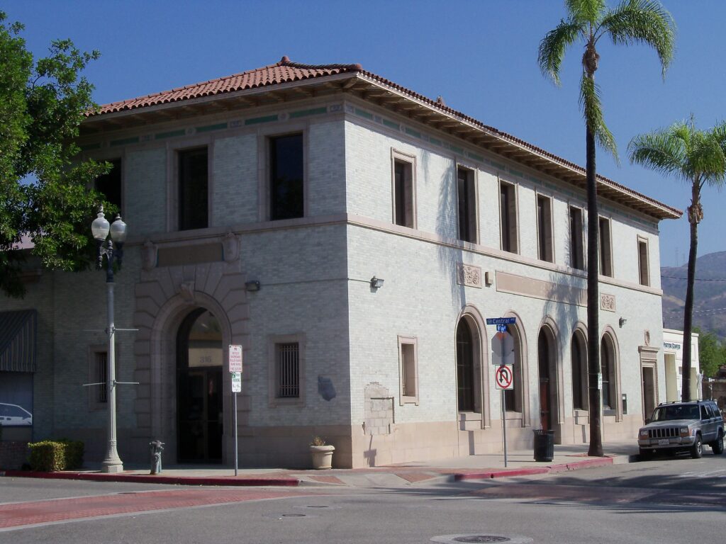 Fillmore State Bank building (2014) features a two-story brick structure with red tile roof, arched windows and doors, marked "316" at entrance, situated at a street corner with Central Ave sign, no parking sign, palm trees, and a parked SUV.