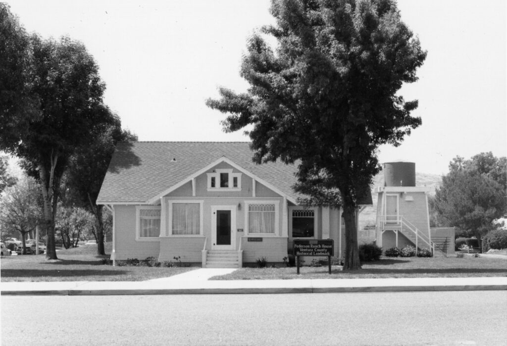 Black-and-white photograph of the Pederson Ranch House, a Ventura County historical landmark, with a water tower and trees, featuring a sign reading "Pederson Ranch House Ventura County Historical Landmark", circa 1980s.