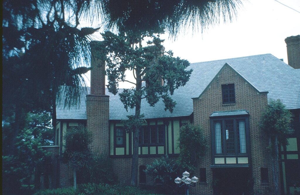 Teague Mansion, a brick Tudor-style house with multiple chimneys, gray shingled roof, and tall windows, surrounded by trees, photographed in 1982.