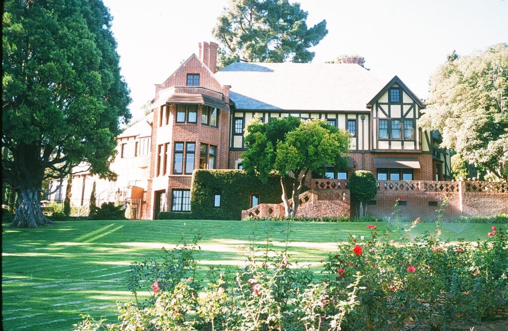 Tudor-style brick mansion with green lawn, trees, and rose bushes, photographed in 1985.