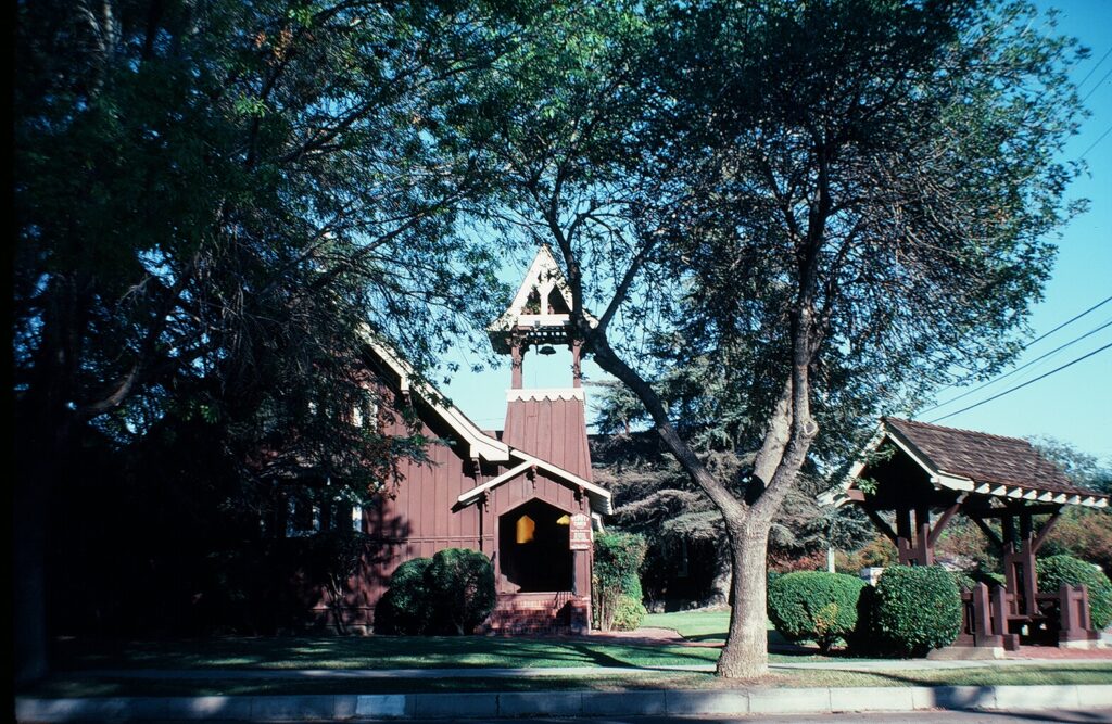Brown wooden Trinity Episcopal Church with bell tower, green lawn, trees, and a covered structure, photographed in 1981.