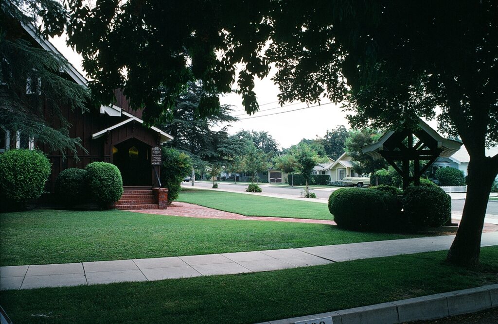 Wooden Trinity Episcopal Church with brick steps, manicured lawn, trees, and sidewalk, 1978.