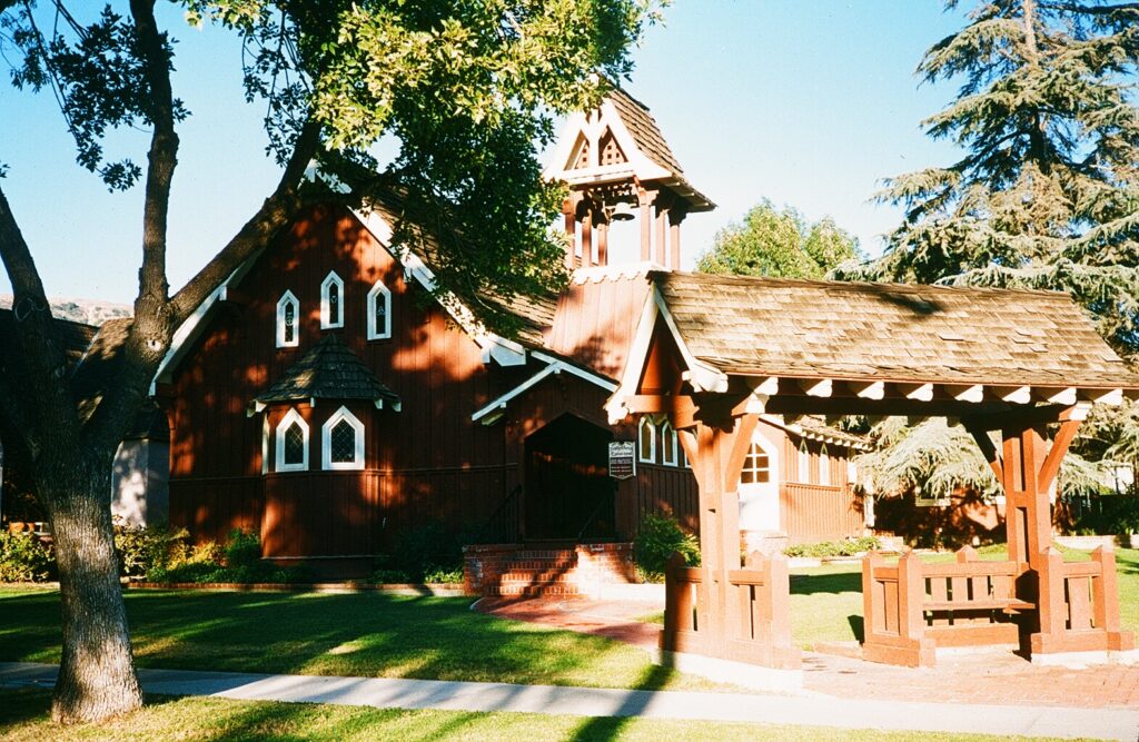 Trinity Episcopal Church from 1985, a redwood building with a bell tower, arched windows, and covered bench on a sunny lawn.