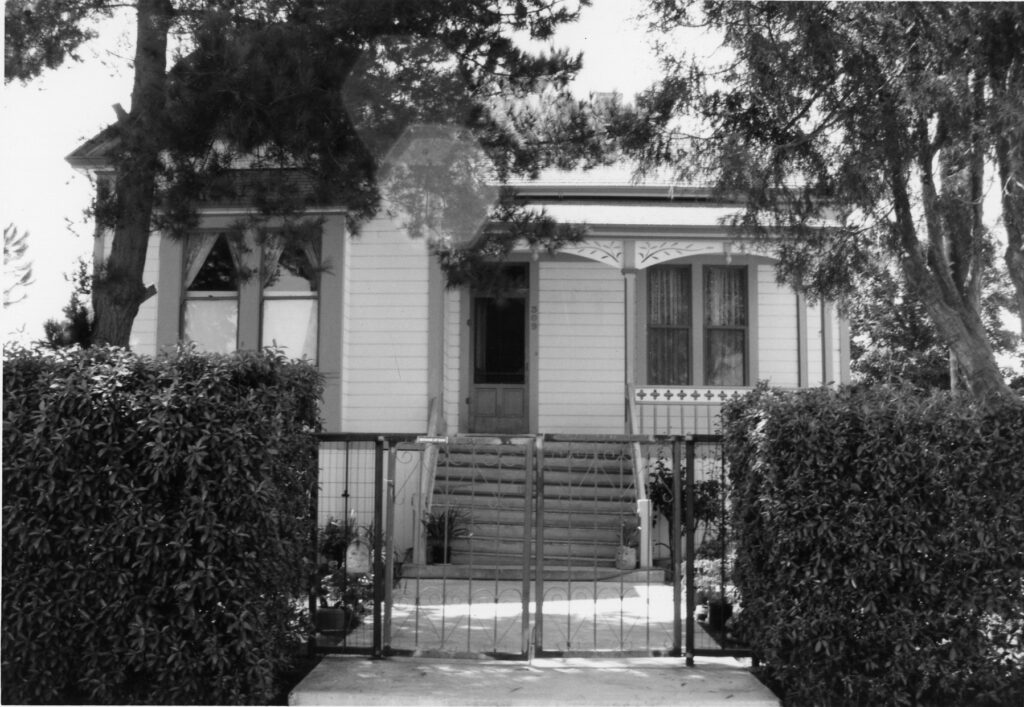Black-and-white photograph of the Wiltfong House, a two-story Victorian-style home with a gated entrance, surrounded by trees and hedges. Visible address number "308" on the facade.
