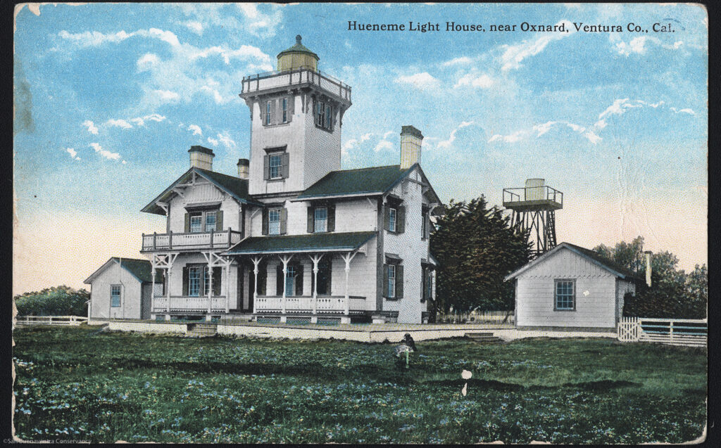 Historical 1874 postcard of Hueneme Lighthouse near Oxnard, Ventura County, California, with visible text "Hueneme Light House, near Oxnard, Ventura Co., Cal." Features a white lighthouse tower attached to a house with porches, small outbuildings, and a water tower on a grassy field under a blue sky.