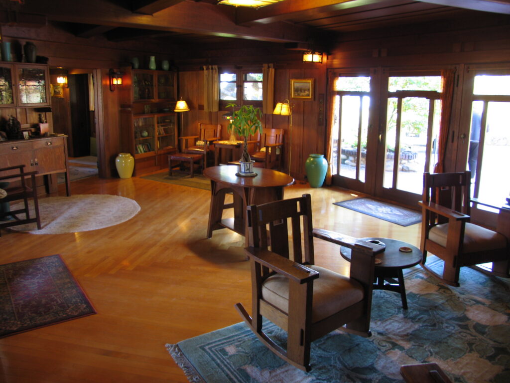 Wood-paneled living room with wooden furniture, rugs, and French doors leading to an outdoor area, photographed in 2007.