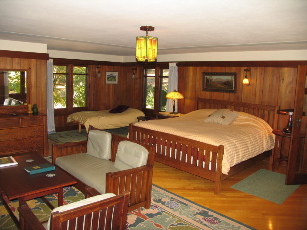 Wooden-paneled bedroom interior from 2007 with two beds, a dresser, and windows overlooking greenery; includes patterned rug, lamps, and seating.
