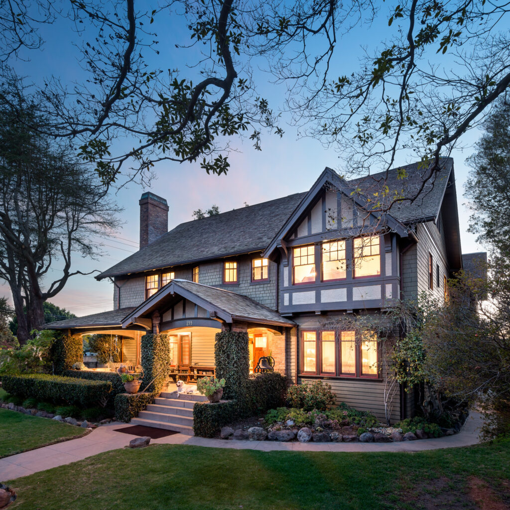 Two-story Tudor-style house with illuminated windows, covered porch, and landscaping; Henry Levy House, 2014, photographed by Stephen Schafer.