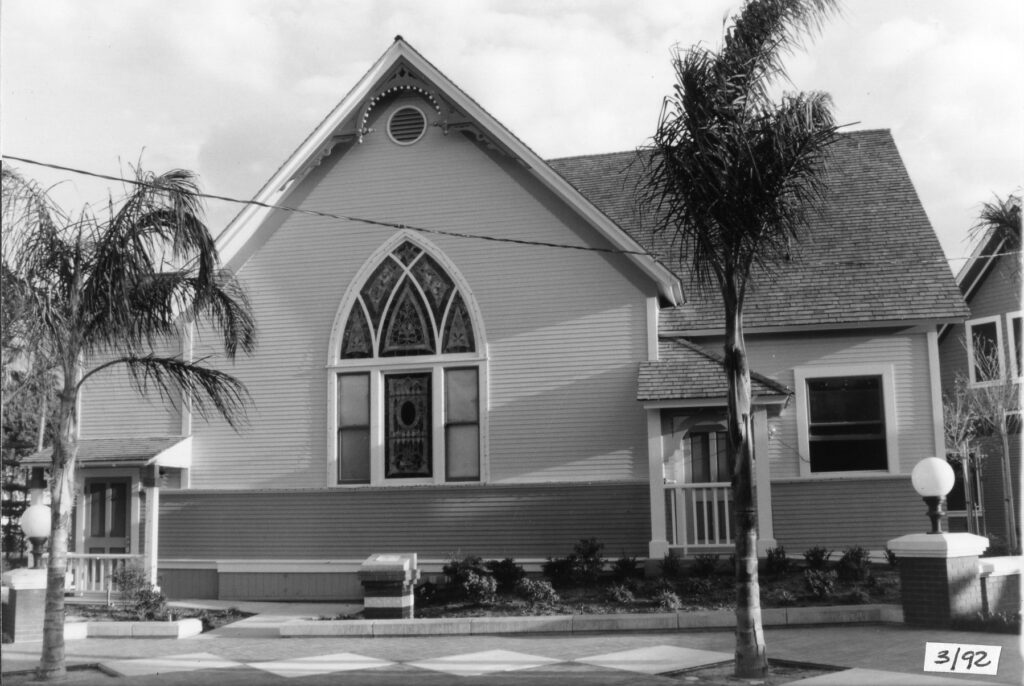 Black-and-white photograph of a church building at Heritage Square, 1992, featuring a Gothic-style window, palm trees, and a paved courtyard. Visible text includes '3/92' in the bottom right corner.