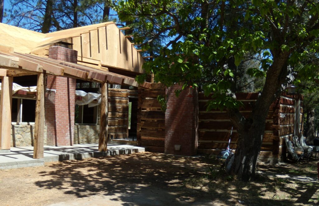 Lathrop Camp building under rehabilitation with exposed wooden framing, brick pillars, stone foundation, and covered patio area surrounded by trees.