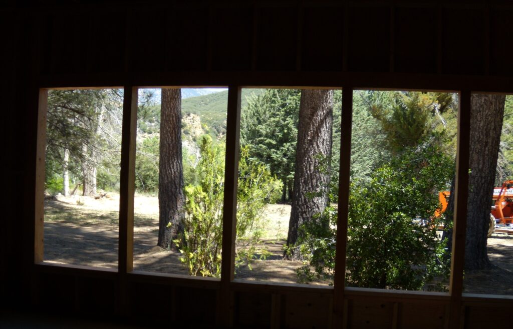 View through a window at Lathrop Camp in 2011, showing a forested landscape with tall trees, a mountain, and an orange vehicle.