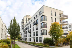 Modern apartment complex with white buildings, black balconies, trees, and bike parking along a pathway.
