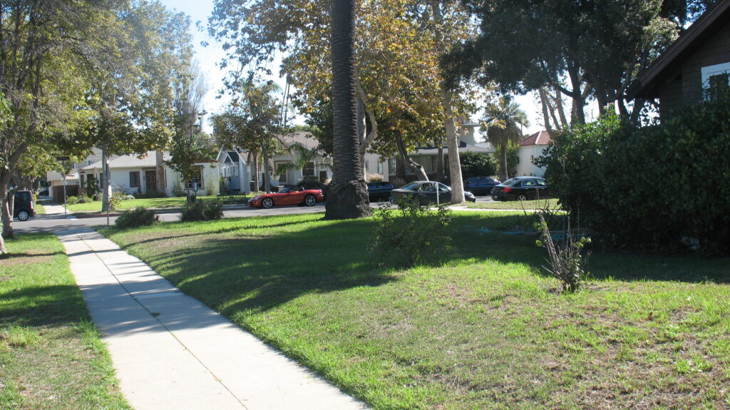 Front yard landscaping of Murphy House (2011) with a concrete sidewalk, grassy area, trees, and parked cars including a red sports car.