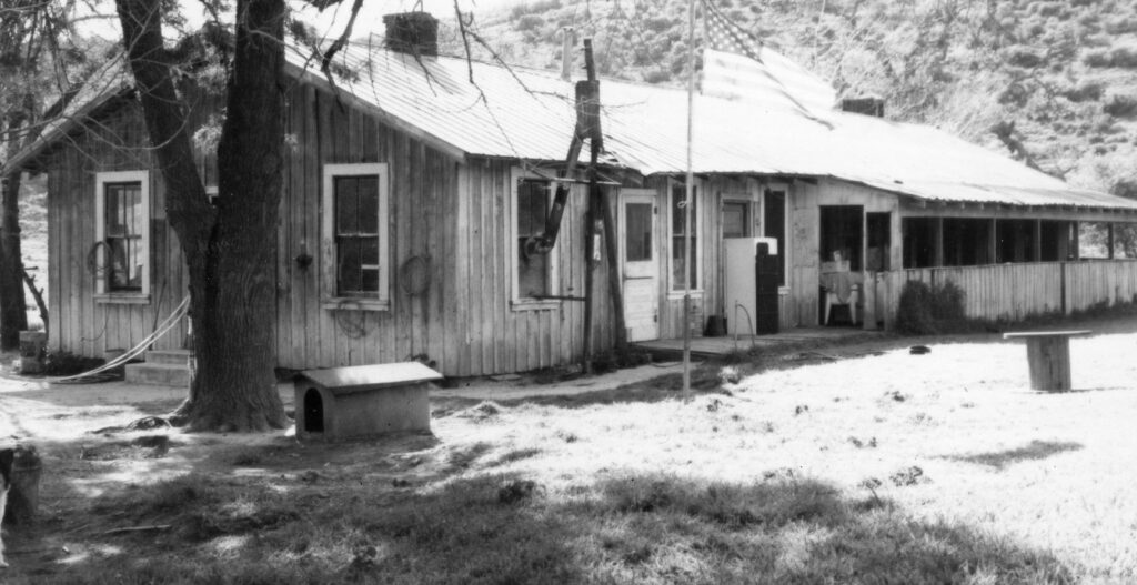 Weathered wooden ranch building with covered porch, trees, and doghouse, part of Patterson Ranch circa 1980s.
