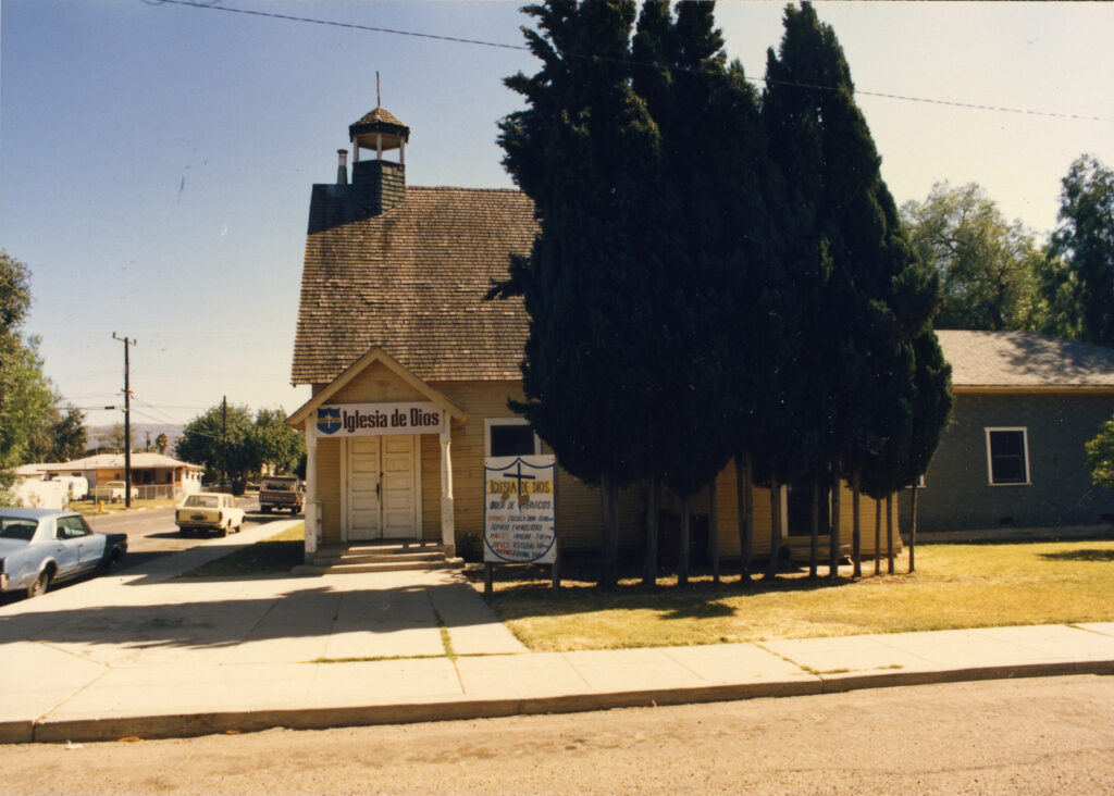 Small yellow church with "Iglesia de Dios" signage, steeple, and sidewalk, identified as Saint Rose of Lima Catholic Church circa 1985.