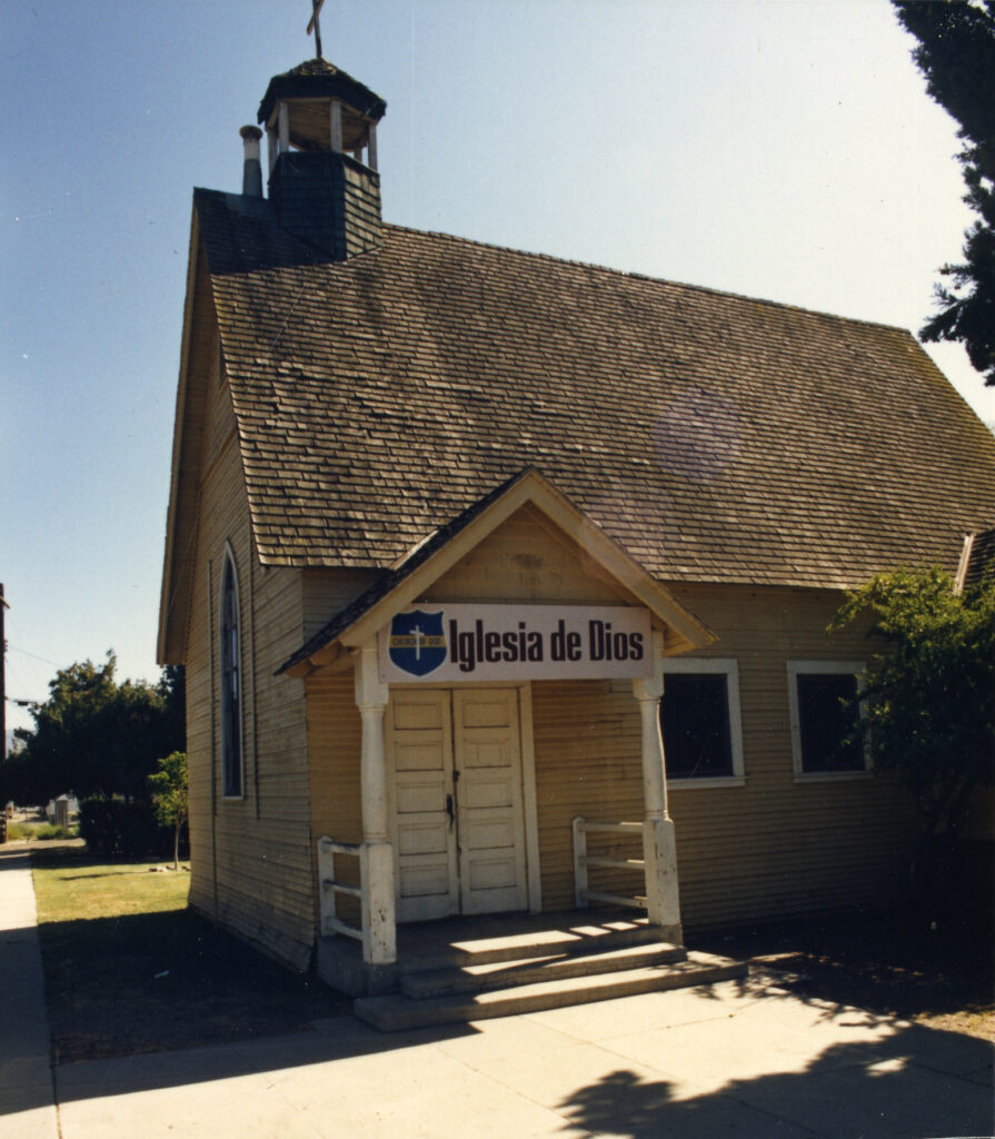 Small wooden church with shingled roof and bell tower, featuring "Iglesia de Dios" sign above double doors, identified as Saint Rose of Lima Catholic Church circa 1985.
