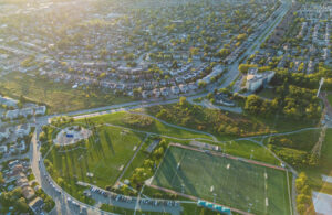 Aerial view of suburban neighborhood with marked soccer and football fields, playground, residential streets, and green spaces illuminated by sunlight.