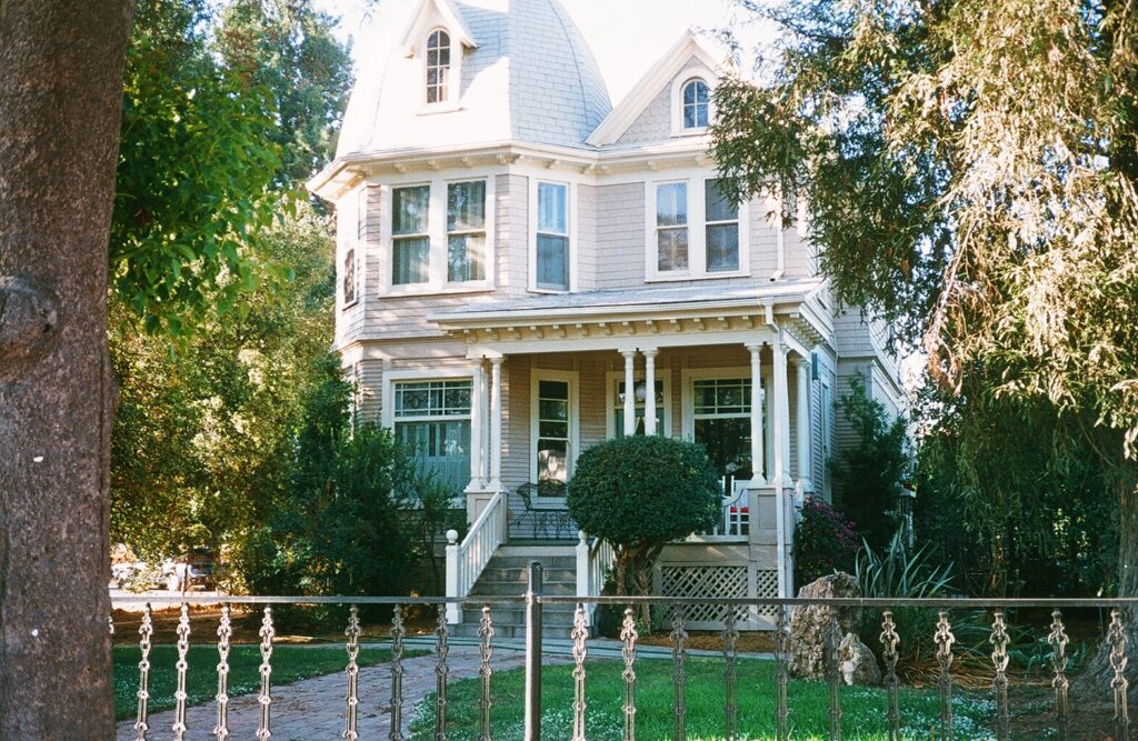 Baker House, a light-colored Victorian-style residence with a wraparound porch, white columns, and surrounding greenery, photographed in 1985.