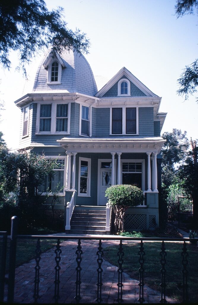 A 1982 Victorian-style house with light blue siding, white trim, a turret, front porch columns, and a brick walkway.