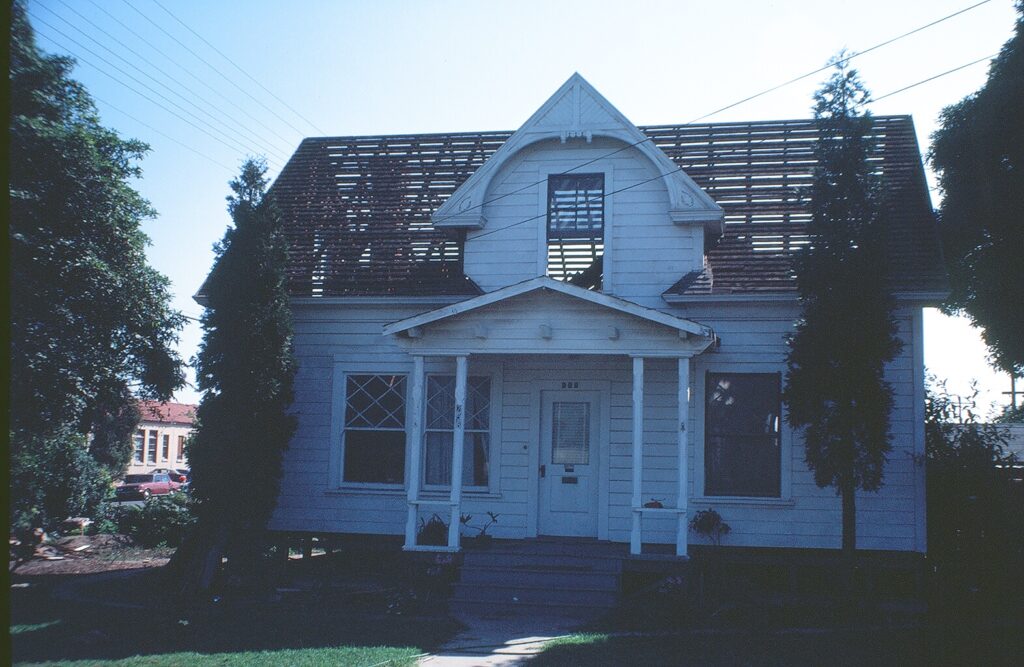 White two-story house with a gabled roof showing missing shingles, a front porch with columns, and trees surrounding the property. Identified as the Gerberding/Moranda House from 1981.