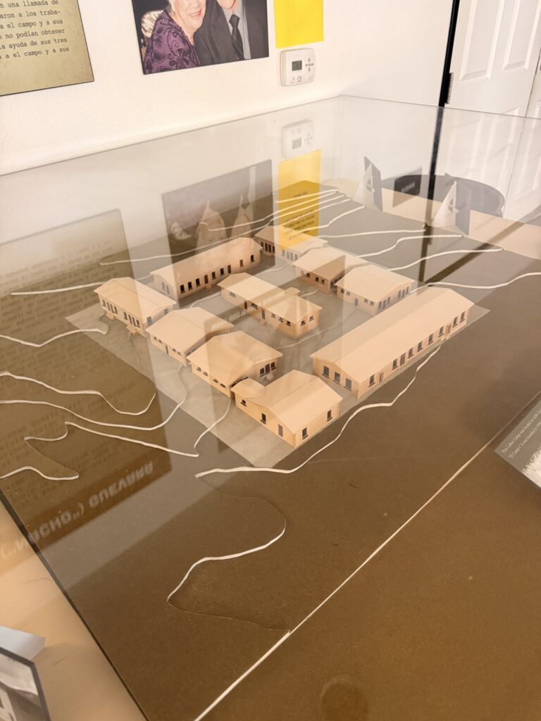 Scale model of the Piru Labor Camp ("El Campo") barracks buildings under a glass display case, part of a bracero history exhibit.
