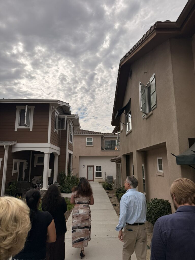 Group of people walking a pathway between two-story residential buildings during a housing development site visit.