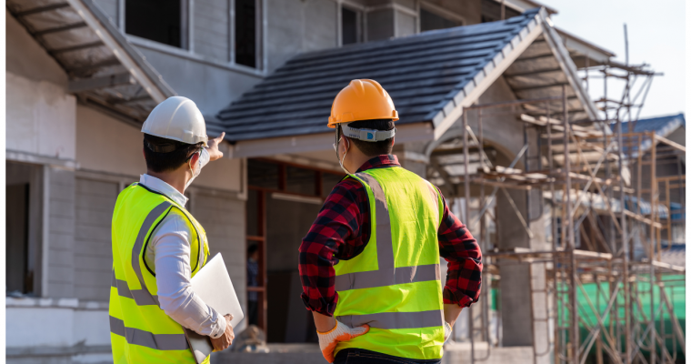 Two construction workers with safety vests and hard hats inspecting a building under construction.