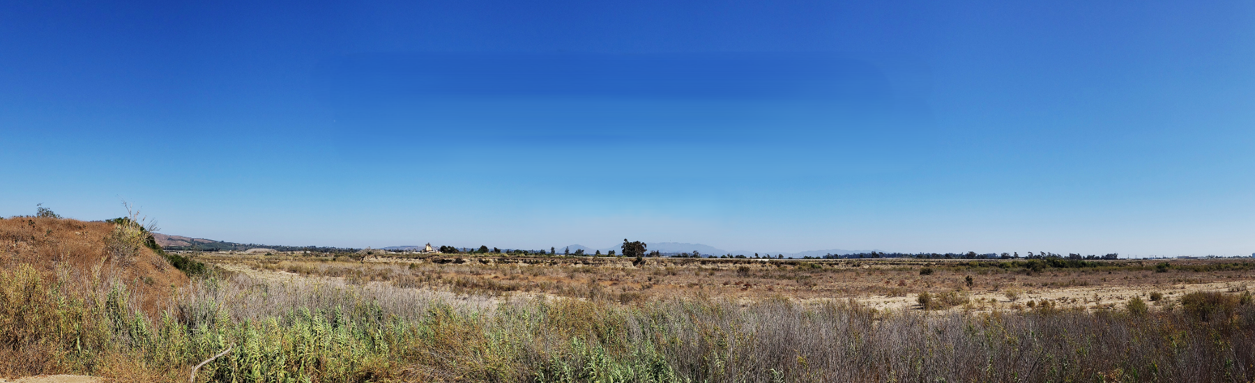 Panoramic view of open valley with clear skies and hills in the distant background. Decorative
