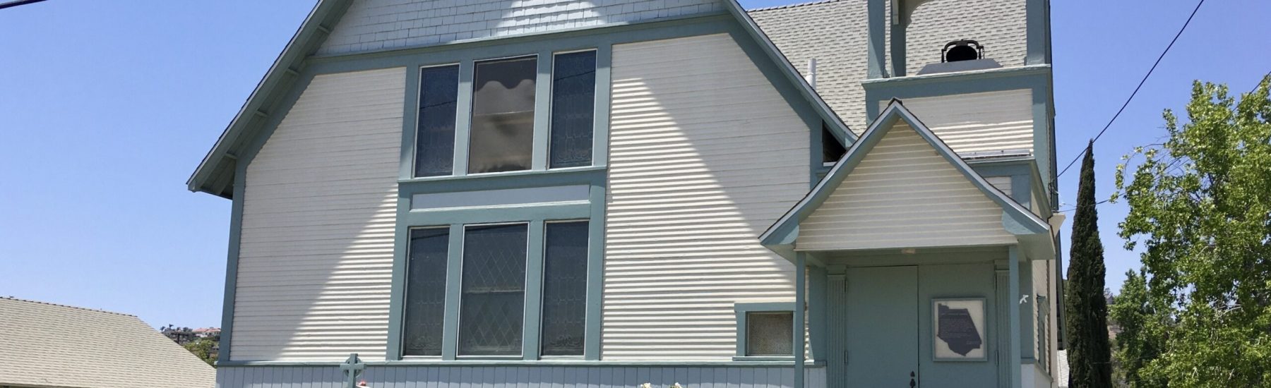 First Christian Church building with light blue and white siding, featuring a steeple, steps to the entrance, and a sign reading "First Christian Church (Disciples of Christ)".