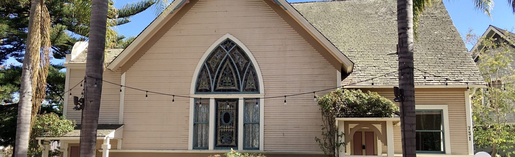 A beige Victorian-style church with a gabled roof and stained glass window at Heritage Square, featuring palm trees, a brick walkway with white squares, and the address number 731 visible on the facade.