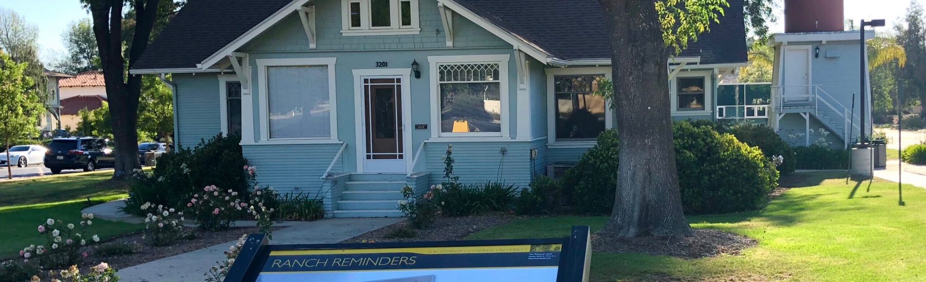 Pederson House, a light blue Victorian-style home with white trim, features a 'RANCH REMINDERS' signboard in the foreground. The house number '3201' is visible above the front door, surrounded by green lawn and trees.