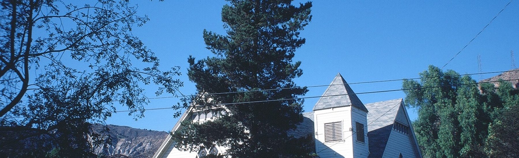White Piru Methodist Church with steeple and arched windows, surrounded by trees and a yellow "Not a Through Street" sign, with mountains in the background, photographed in 1981.