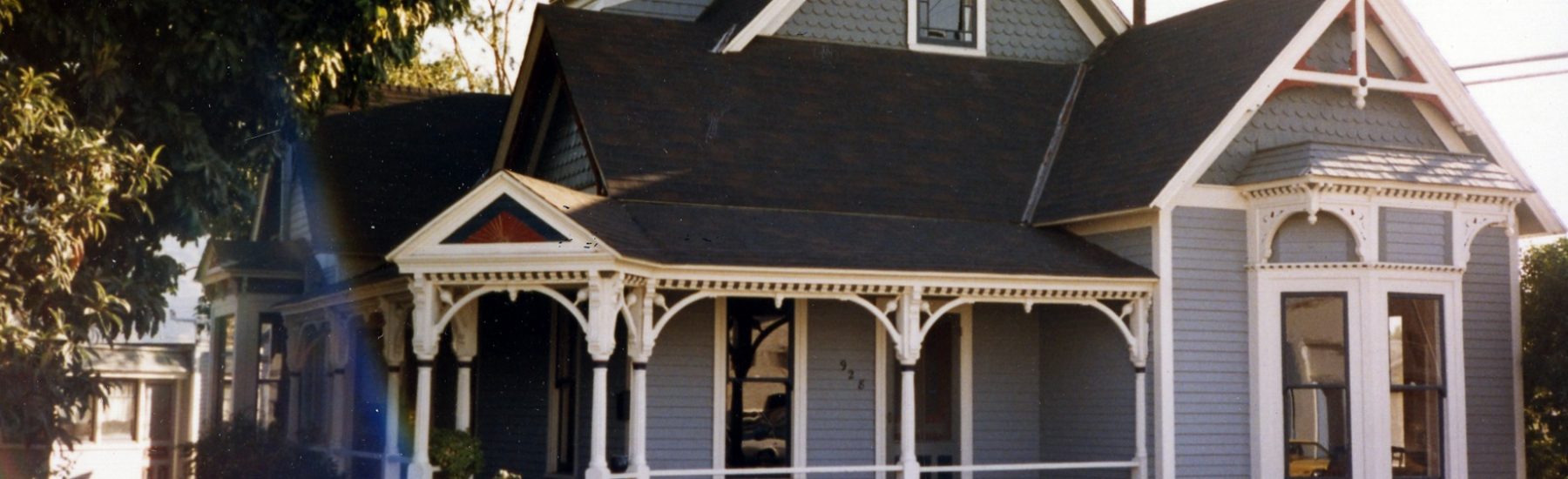 Rice House, a light blue Victorian home with white trim, wraparound porch, and white picket fence, circa 1980s. Address number 928 visible on the sidewalk.
