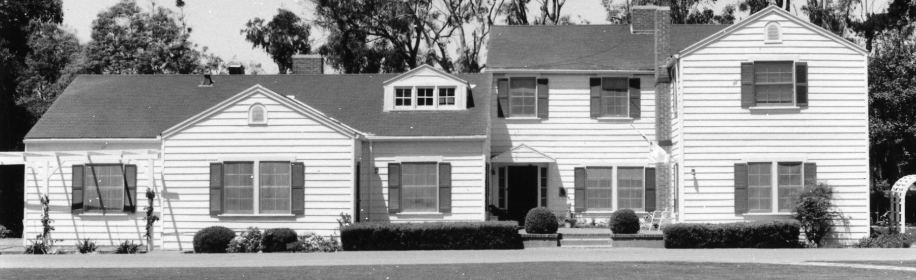 A large white two-story house with dormer windows, shutters, and a landscaped lawn, identified as the Richard Bard House from the 1980s.