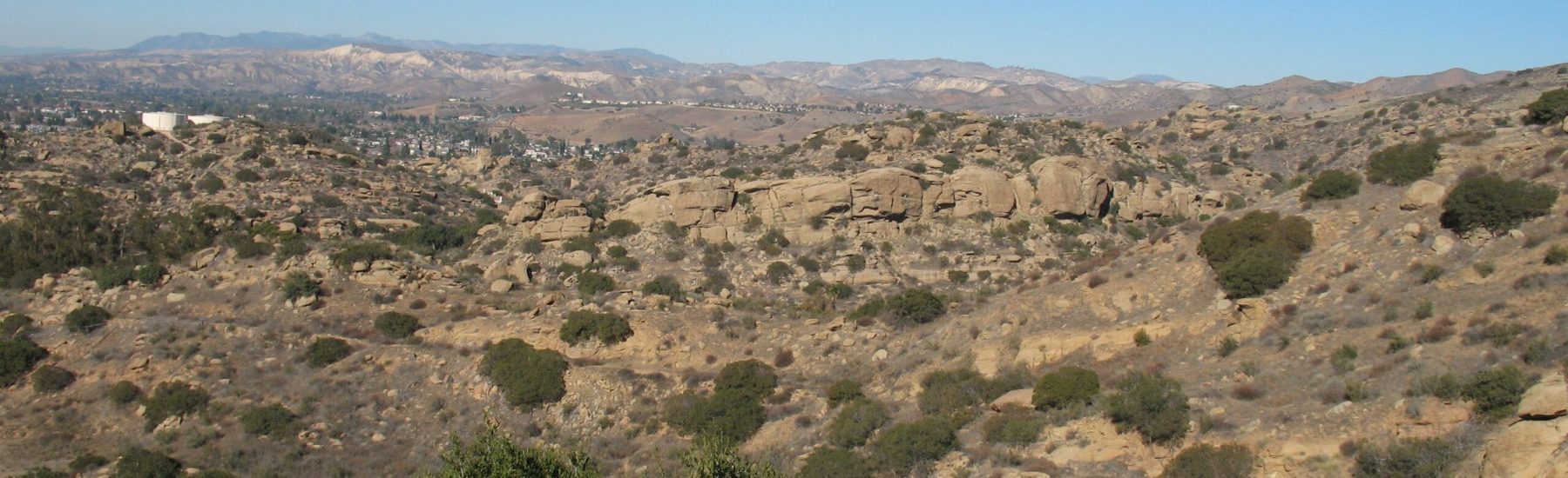 Rocky hillside with scattered shrubs and distant mountains under a clear blue sky, depicting the historical Freight Road in Simi Hills, 2016.